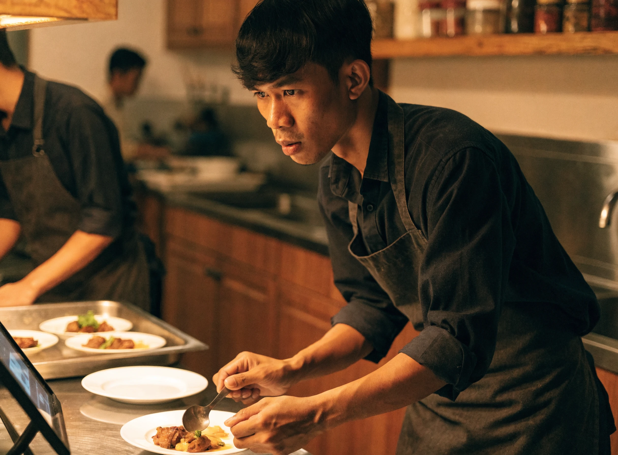 Chef melihat skrin kitchen display sambil menghidang makanan