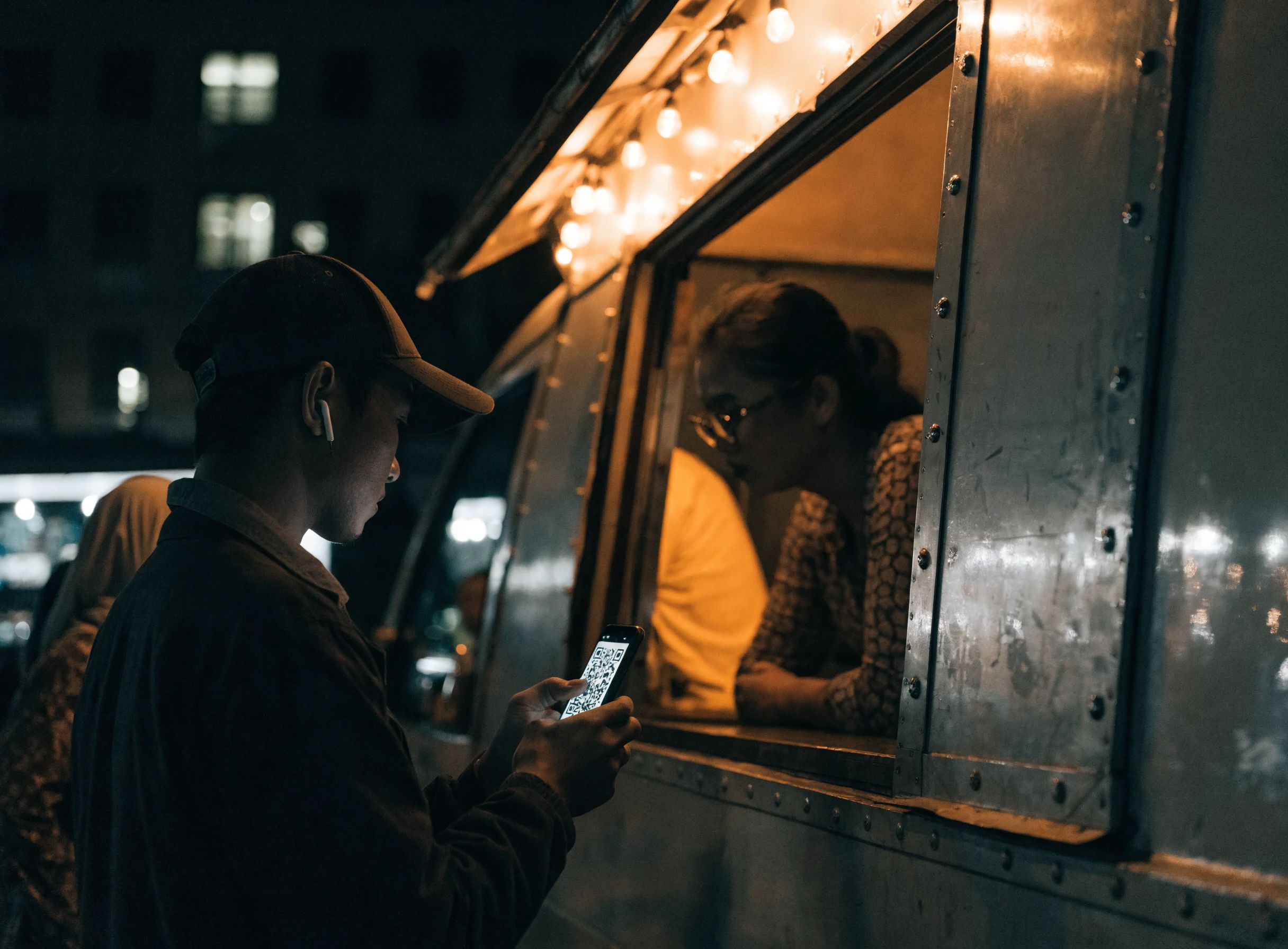 Pelanggan membayar dengan mengimbas kod QR di tingkap food truck pada waktu malam