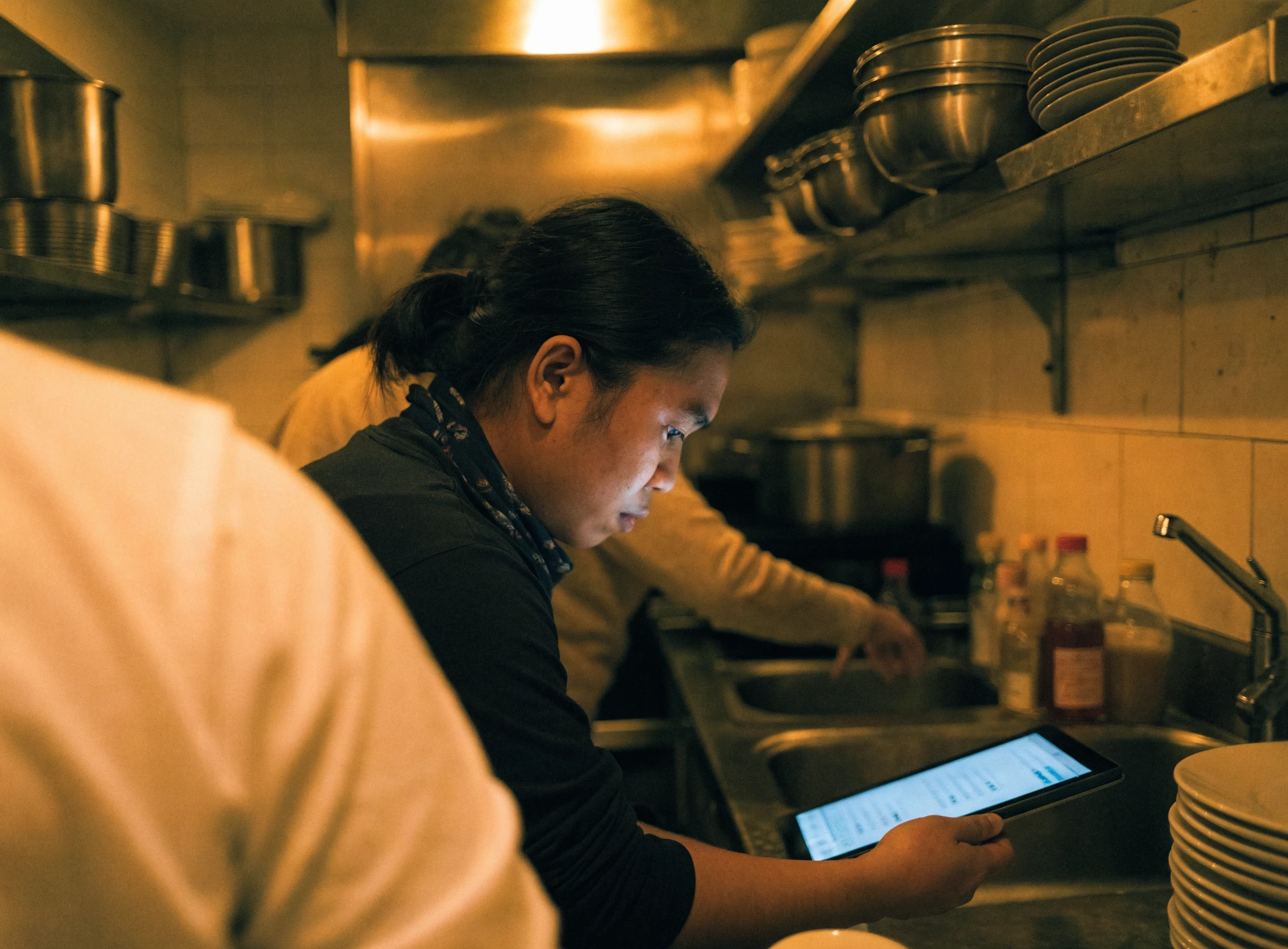 Staf dapur melihat skrin tablet menunjukkan order masuk